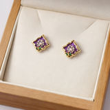 Pair of purple flower-shaped earrings with gold accents on a white cushion in a wooden box.
