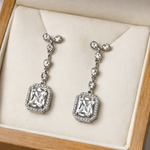 Pair of silver earrings with clear gemstones on a beige cushion