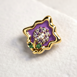 Decorative brooch with purple center, gold border, and green accents on a white background