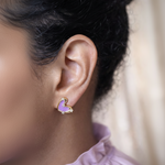 Close-up of an ear wearing a purple heart-shaped earring with gold accents.